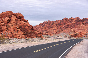 Overton, Nevada, USA - February 24, 2010: Valley of Fire. New black asphalt road with yellow line divider on dry desert floor meanders between red rock hills under thick light blue cloudscape.