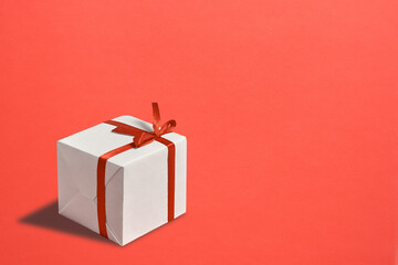 White gift box with red ribbon on a bright red background. Copy space.