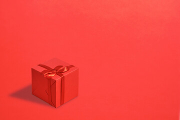 Bright red gift box with ribbon on a red background. Copy space.