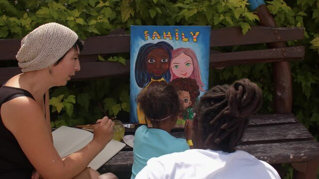 Sunny summer day for creative fantasy and creativity. Black man and caucasian woman with biracial girl paint a family portrait on canvas outdoor. 