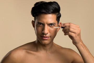 Studio portrait of shirtless man applying foundation under eye