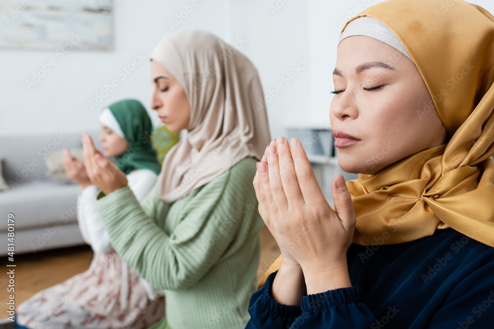 Wall mural asian woman praying near blurred muslim daughter and granddaughter at home.