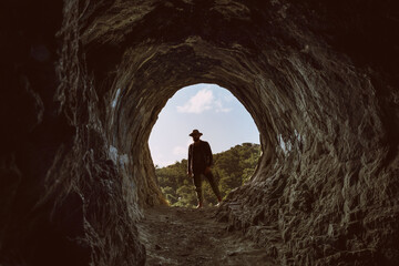 Portrait of a 30s man with a fedora and shirt at the entry of the Homer's cave