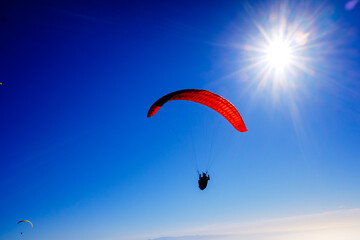 Paragliding above mountain peaks and white clouds during winter blue sunny day.