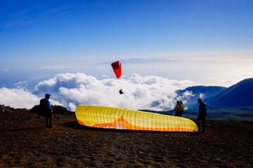 Skydiving experts and monitors prepare the sail of a paraglider to fly over the clouds of the...