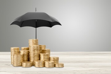 Holding a small umbrella over a pile of coins on the table. Financial safety and investment concept. © BillionPhotos.com