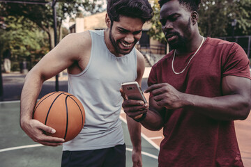 USA, Pennsylvania, Philadelphia, Friends looking at smart phone in basketball court