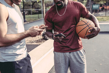 USA, Pennsylvania, Philadelphia, Two men with basketball balls holding smart phones - obrazy, fototapety, plakaty