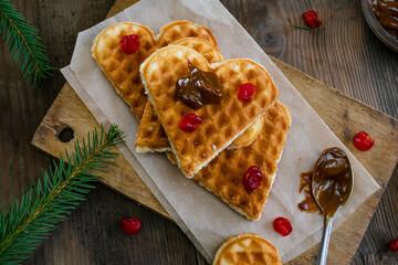 Homemade Belgian waffles heart shaped on plate with colorful red sweet cherry berries, banana, and boiled condensed milk, dessert food. background for Valentines day, womens day, love, romance