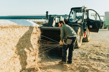 a man picking up the strings of a hay bales after cutting them. © Samuel Perales