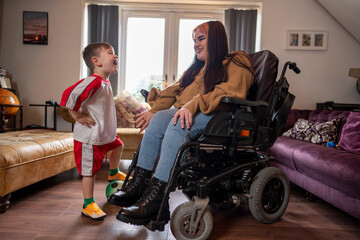 Woman on wheelchair with son in soccer uniform in living room