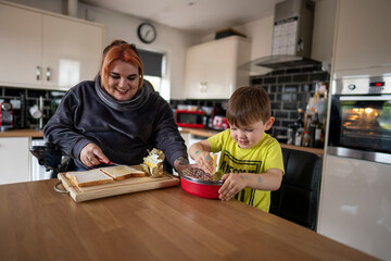 Mother in wheelchair and son making toasts in kitchen