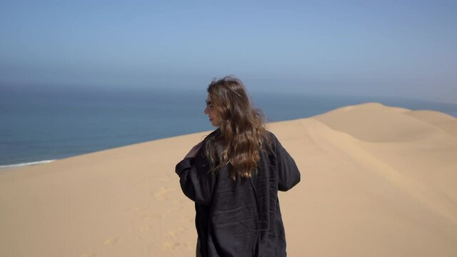 A young woman walks along sandy dunes on seashore. Sandwich Harbour in Namibia.