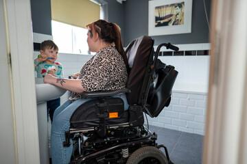 Mother in wheelchair with son brushing teeth in bathroom - obrazy, fototapety, plakaty