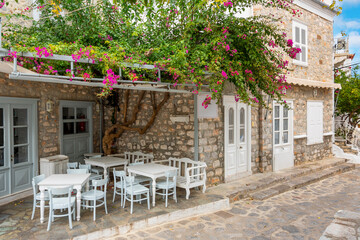 A small patio with tables and chairs in a picturesque alley of Bougainvillea flowers on the Greek Island of Hydra, Greece.