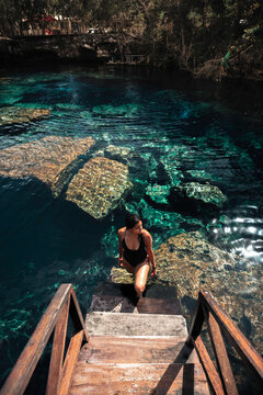 Mujer joven, atractiva, latina en bikini, parada en la escalera de un cenote cristalino, cerca de Tulum M&eacute;xico