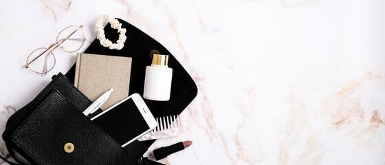 Elegant women's handbag with smartphone, paper notebook, scrunchy, glasses on marble table. Beauty blog banner design. Flat lay, top view, copy space.