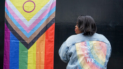 Mature woman wearing denim jacket in front of pride flag