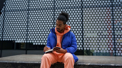 Young man sitting by fence and writing in notepad © Cultura Creative