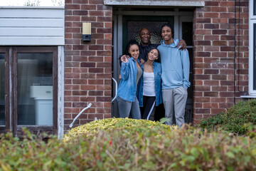 Portrait of family with teenage daughter and son in doorway of new house