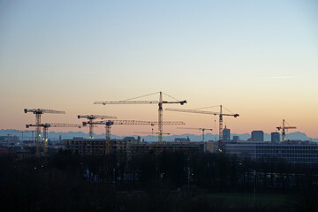 sunset munich with cranes and the alps - obrazy, fototapety, plakaty