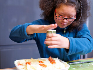 Girl with Down Syndrome seasoning dish in kitchen