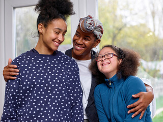 Smiling mother embracing two daughters at home