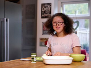 Portrait of smiling girl with Down Syndrome preparing food in kitchen