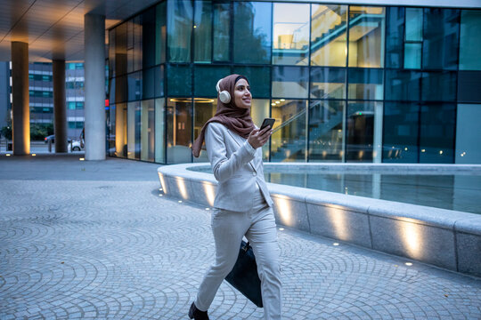UK, London, Businesswoman in hijab and headphones walking in city