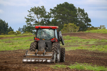 A small tractor with a power harrow breaks up the soil and clods and prepares it for a new crop or orchard trees. North Island, New Zealand