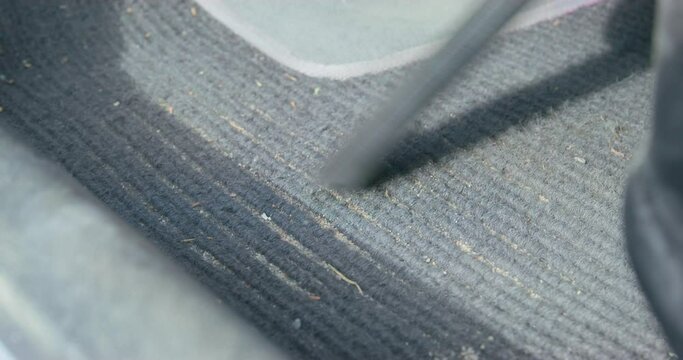 Person carefully vacuums every crevice in dirty fabric car mat with vacuum cleaner with special long thin nozzle, close up. Professional detailing and dry cleaning of car interior.