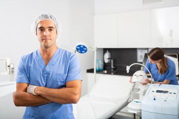 Obraz premium Portrait of positive man doctor of clinic of aesthetic medicine wearing blue overall meeting client