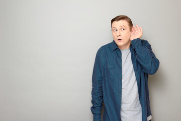 Portrait of curious man placing hands near his ears and eavesdropping