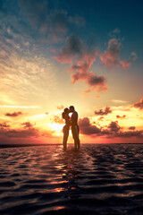 Silueta de una pareja de jóvenes enamorados besándose al amanecer en playa, contraluz