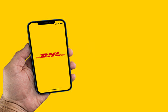 Male hand holding a smartphone with DHL International package delivery and express mail service app on the screen. Yellow background. Rio de Janeiro, RJ, Brazil. January 2022