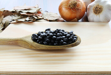 Black beans spoon with onion, garlic bulb and bay leaves in the background.