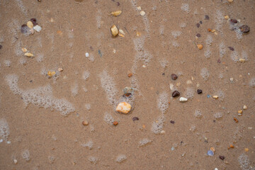Myriad of pebbles with wave foams on a beach. Selective focus points