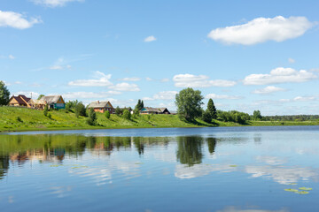 Fototapeta na wymiar Idyllic rural landscape. Small village by the lake on a sunny summer day. The clouds are reflected in the lake