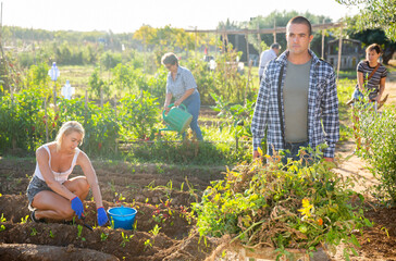 Positive man gardener carrying plants in wheelbarrow at homestead