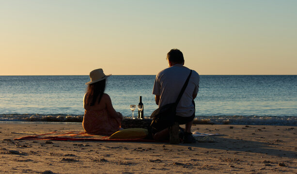A couple having a glass of wine at sunset on Port Willunga Beach, Fleurieu Peninsula, South Australia.