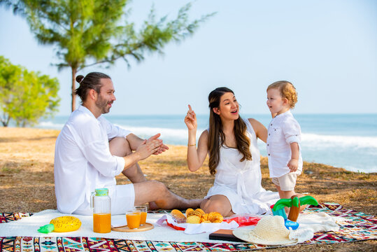 Caucasian couple picnic party with little child boy together on tropical beach. Happy family father and mother with cute baby son enjoy and fun outdoor activity lifestyle on summer travel vacation