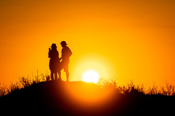 Silhouette of a man and a woman on a hill at sunset.