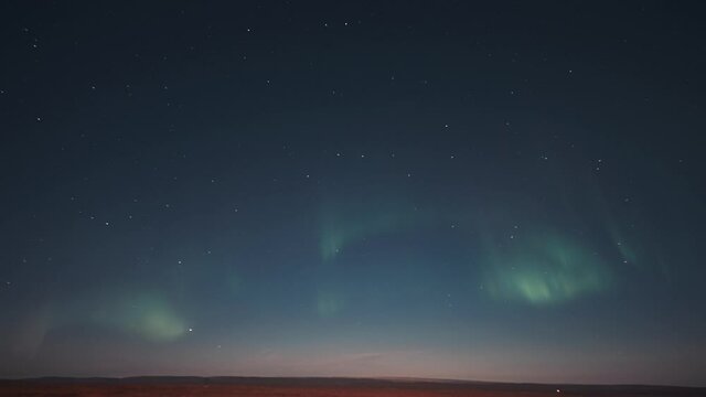 A timelapse of the beautiful dance of the pale and gentle lights of the aurora on the night sky above the tundra.