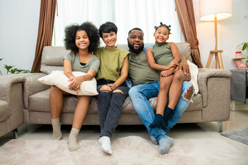 Portrait of Happy African family parents and two little daughter sitting on sofa in living room playing together. Father and mother with child girl kid enjoy indoor lifestyle activity together at home