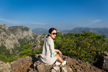 Asian woman with sunglasses sit on the top of the mountain.