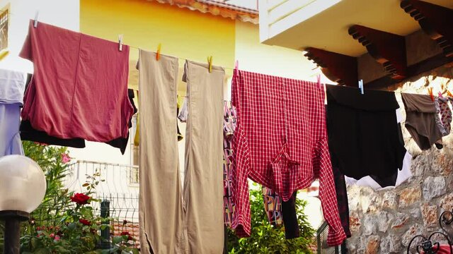 Clothes hang on a line in a row after being cleaned up outside and trembling on the wind at summer day. Trousers and shirts are attached by clothespin after washing. Concept of the laundry and textile