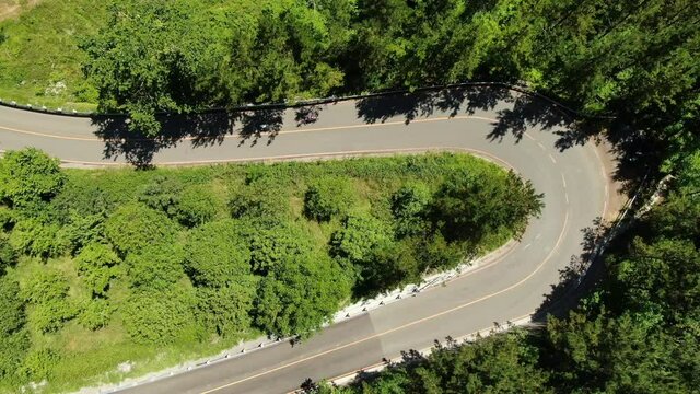 Aerial view of three cyclists riding downhill, taking advantage of a u-turn to overtake his competitor (drone shot) 