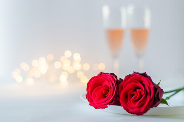 Red roses on plate with glasses of sparkling Rose wine on white background with bokeh light for anniversary and Valentine's day concept.