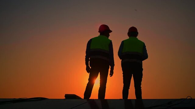 Silhouette engineers walking on roof inspect and check solar cell panel by hold equipment box and radio communication ,solar cell is smart grid ecology energy sunlight alternative power concept.