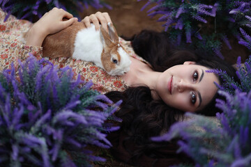 Young brunette woman laying in lavender with rabbit on her chest